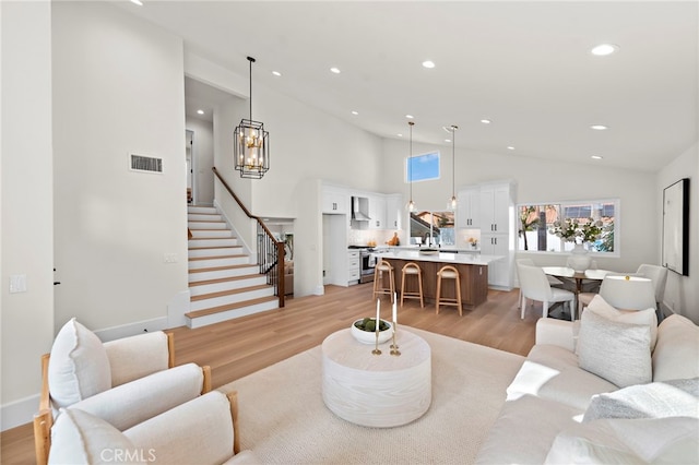 living room featuring an inviting chandelier, sink, light hardwood / wood-style floors, and high vaulted ceiling