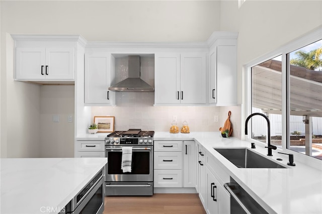 kitchen featuring stainless steel appliances, sink, wall chimney range hood, and white cabinets