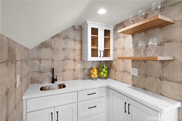 kitchen with white cabinetry, lofted ceiling, sink, and tile walls