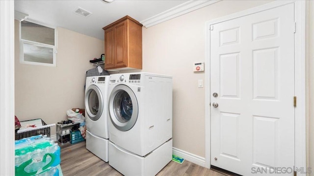 clothes washing area with washer and clothes dryer, light hardwood / wood-style floors, and cabinets