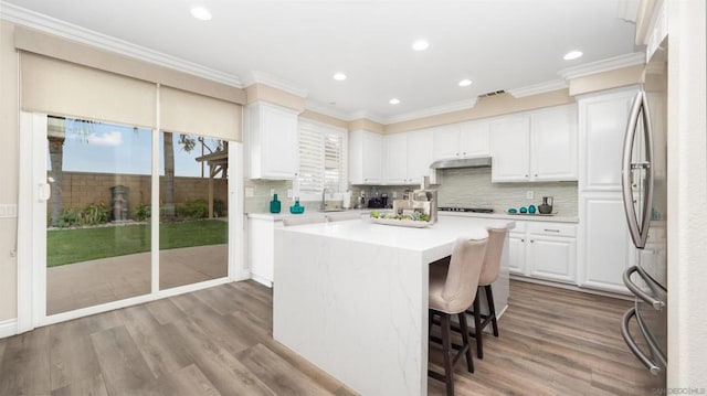 kitchen with crown molding, stainless steel refrigerator, white cabinets, and a center island