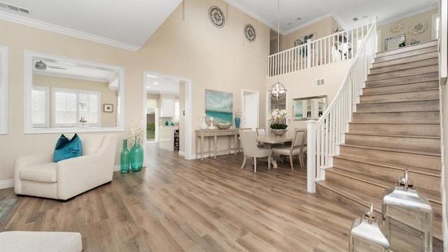 living room with crown molding, wood-type flooring, ceiling fan with notable chandelier, and a towering ceiling