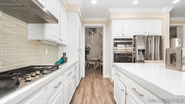 kitchen featuring white cabinetry, ventilation hood, ornamental molding, stainless steel appliances, and decorative backsplash