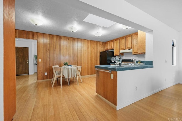 kitchen with a skylight, black refrigerator, light hardwood / wood-style floors, and kitchen peninsula