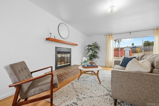 living room featuring vaulted ceiling, a brick fireplace, and light hardwood / wood-style flooring