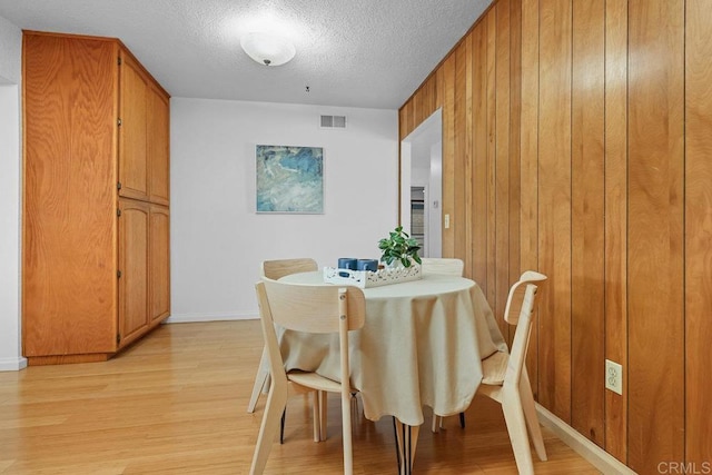 dining area with a textured ceiling, light hardwood / wood-style floors, and wood walls