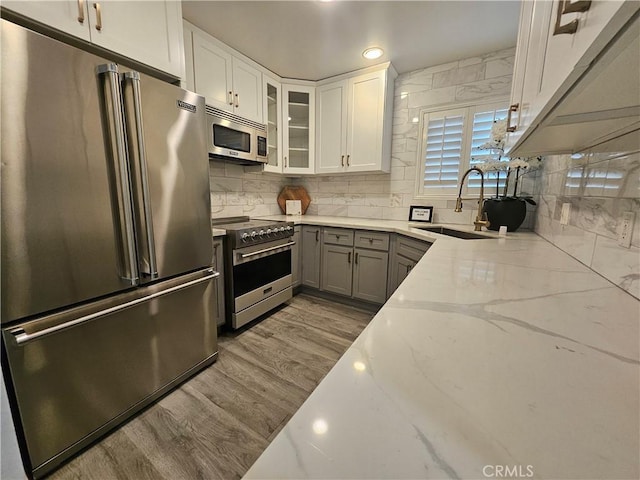 kitchen featuring high quality appliances, sink, backsplash, white cabinets, and light stone counters