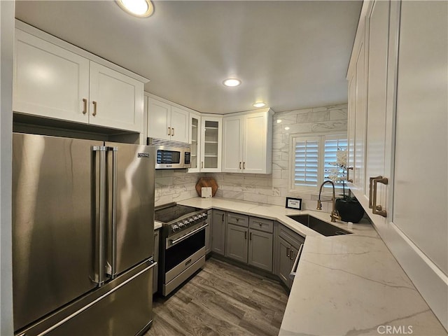 kitchen with premium appliances, light stone countertops, sink, and white cabinets