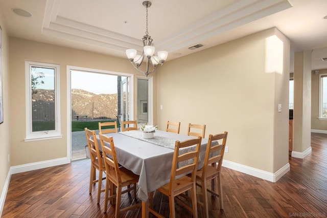 dining room featuring dark hardwood / wood-style flooring, a mountain view, a raised ceiling, and an inviting chandelier