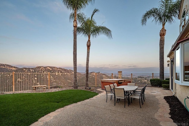 patio terrace at dusk featuring a yard, a hot tub, and a mountain view