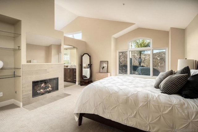 carpeted bedroom featuring a tiled fireplace, connected bathroom, and high vaulted ceiling