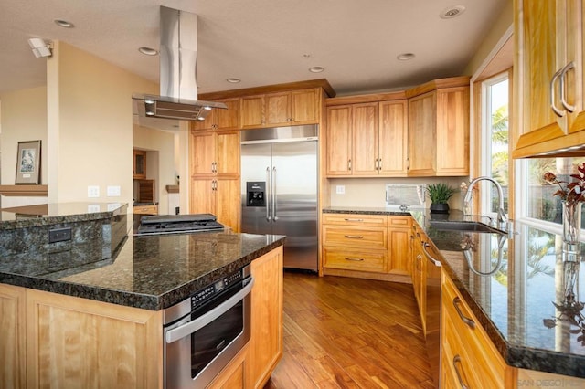 kitchen with dark stone countertops, appliances with stainless steel finishes, sink, and island range hood