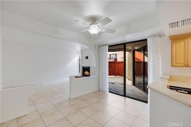 unfurnished living room featuring baseboards, visible vents, light tile patterned flooring, a warm lit fireplace, and ceiling fan