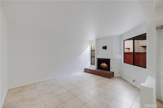 unfurnished living room with light tile patterned floors, baseboards, and a lit fireplace