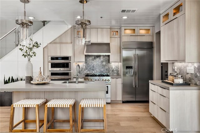 kitchen with high end appliances, sink, hanging light fixtures, and a center island with sink