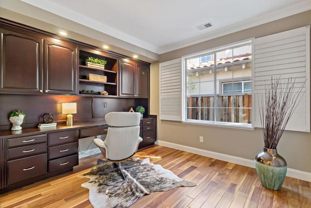 office area with built in desk, ornamental molding, and light wood-type flooring