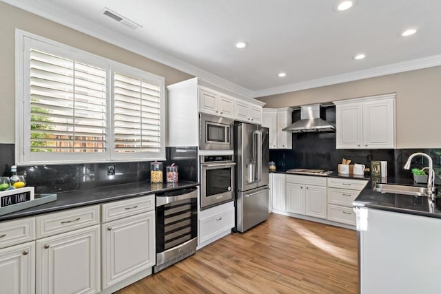 kitchen featuring appliances with stainless steel finishes, white cabinetry, sink, wine cooler, and wall chimney exhaust hood