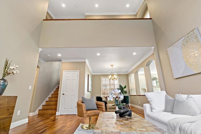 living room with an inviting chandelier, hardwood / wood-style flooring, ornamental molding, and a towering ceiling