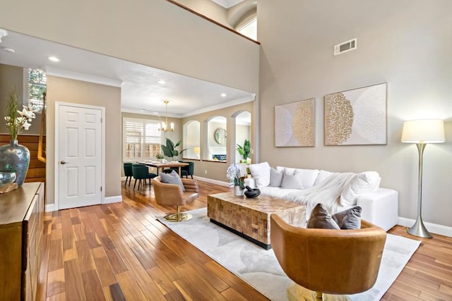 living room with a towering ceiling, ornamental molding, light hardwood / wood-style flooring, and a notable chandelier