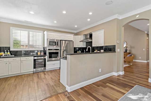 kitchen featuring wall chimney range hood, white cabinetry, stainless steel appliances, wine cooler, and ornamental molding