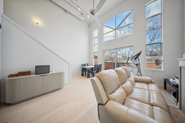 living room with ceiling fan, rail lighting, light hardwood / wood-style floors, and a towering ceiling