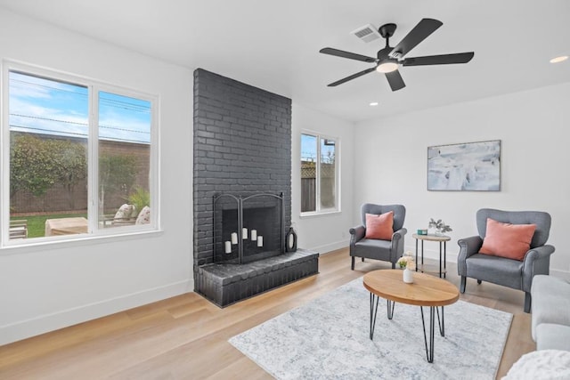 living room with a brick fireplace, ceiling fan, and light hardwood / wood-style flooring