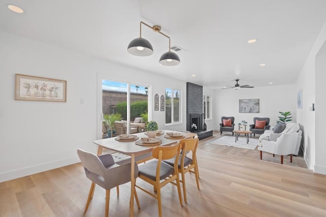 dining area with ceiling fan, light wood-type flooring, and a fireplace