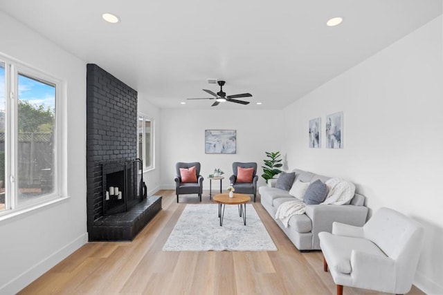 living room with ceiling fan, a fireplace, and light hardwood / wood-style floors