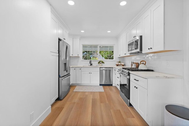 kitchen featuring appliances with stainless steel finishes, sink, white cabinets, backsplash, and light hardwood / wood-style flooring