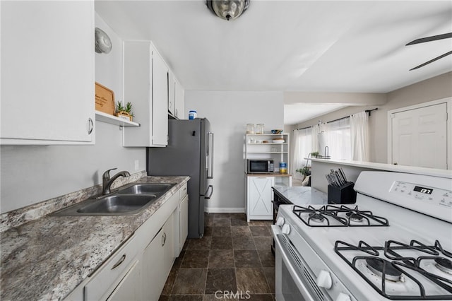 kitchen featuring sink, stainless steel fridge, white cabinets, ceiling fan, and gas range gas stove