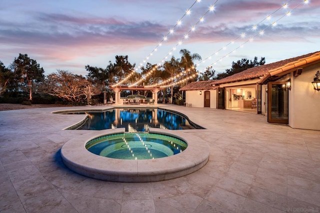 pool at dusk featuring a patio area and an in ground hot tub