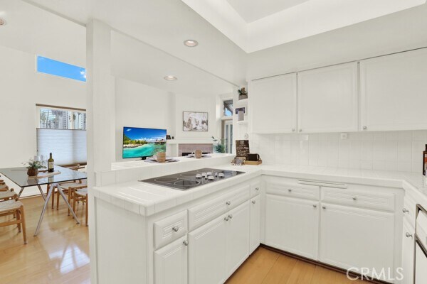 kitchen with tasteful backsplash, white cabinetry, tile counters, kitchen peninsula, and black electric cooktop