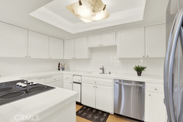 kitchen featuring white cabinetry, tile countertops, a raised ceiling, and appliances with stainless steel finishes