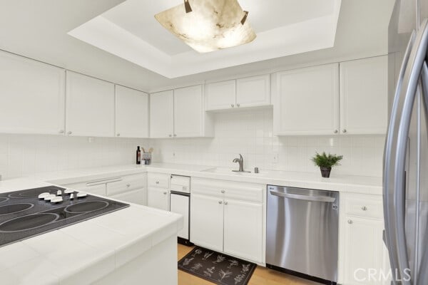 kitchen featuring tile countertops, appliances with stainless steel finishes, and a raised ceiling