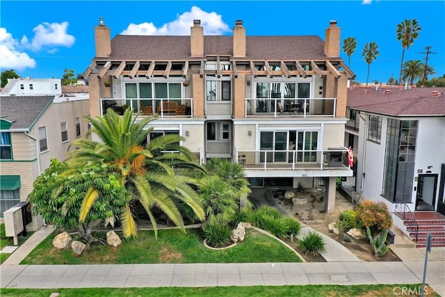 rear view of property featuring a chimney, roof with shingles, and a balcony