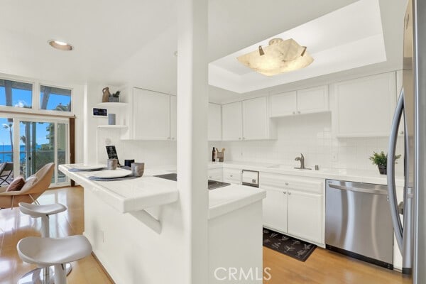 kitchen featuring sink, light wood-type flooring, appliances with stainless steel finishes, decorative backsplash, and white cabinets