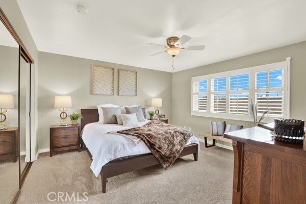 bedroom with a ceiling fan, a closet, light colored carpet, and baseboards