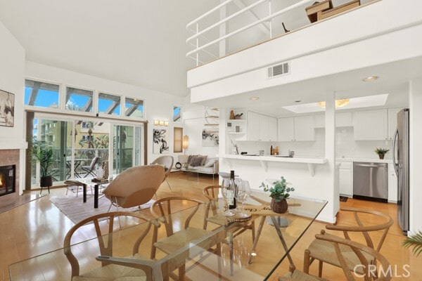 dining room featuring a towering ceiling, light wood-style floors, visible vents, and a glass covered fireplace