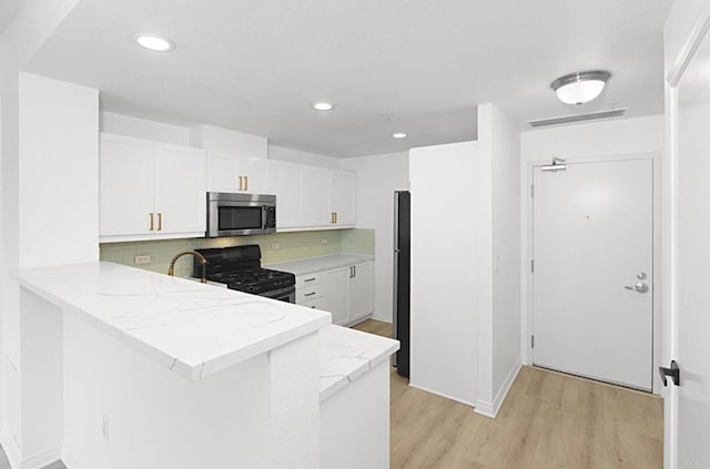 kitchen with white cabinetry, backsplash, stainless steel appliances, kitchen peninsula, and light wood-type flooring