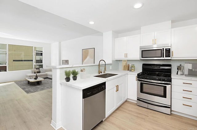 kitchen featuring white cabinets, appliances with stainless steel finishes, open floor plan, light wood-type flooring, and a sink