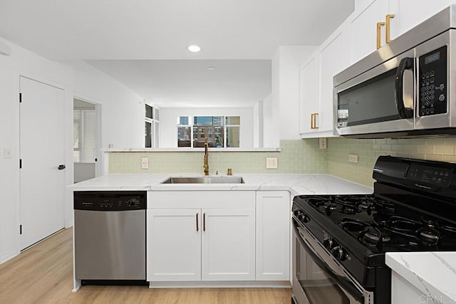 kitchen featuring white cabinets, light stone countertops, stainless steel appliances, and a sink