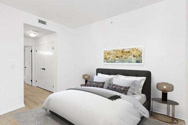 bedroom with light wood-type flooring, baseboards, visible vents, and a closet