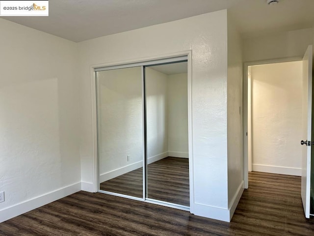 unfurnished bedroom with dark hardwood / wood-style flooring and a closet