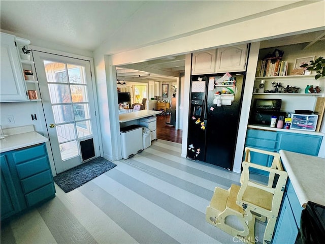 kitchen with lofted ceiling, black fridge with ice dispenser, blue cabinets, and light wood-type flooring