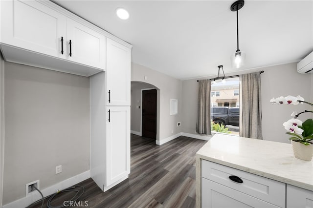 kitchen featuring pendant lighting, white cabinetry, a wall mounted AC, dark hardwood / wood-style flooring, and light stone countertops