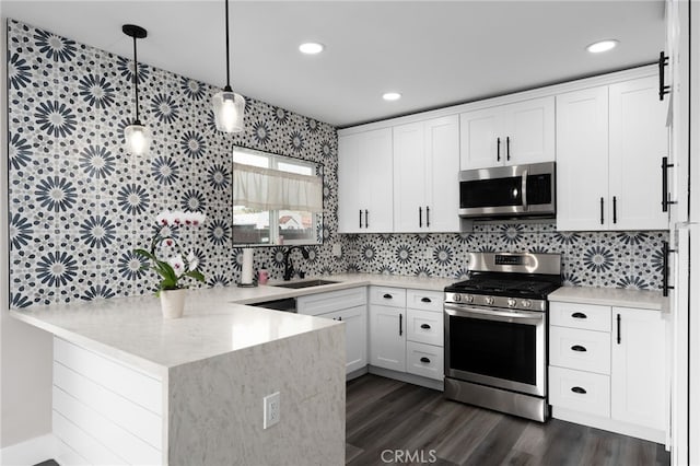 kitchen with appliances with stainless steel finishes, white cabinetry, pendant lighting, and kitchen peninsula