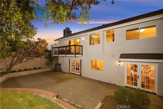 back house at dusk featuring a balcony, a patio area, central air condition unit, and french doors