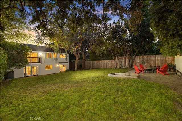 yard at dusk with cooling unit, a balcony, a patio area, and a fire pit