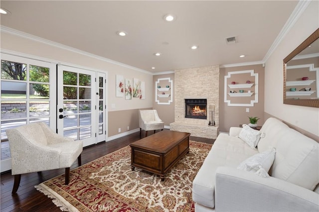 living room featuring dark hardwood / wood-style flooring, crown molding, a stone fireplace, and french doors