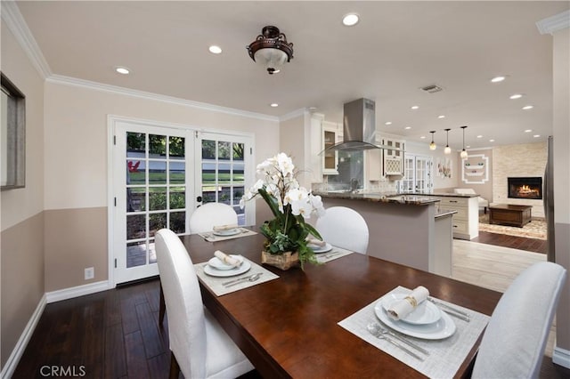 dining space with dark hardwood / wood-style flooring, crown molding, and a large fireplace